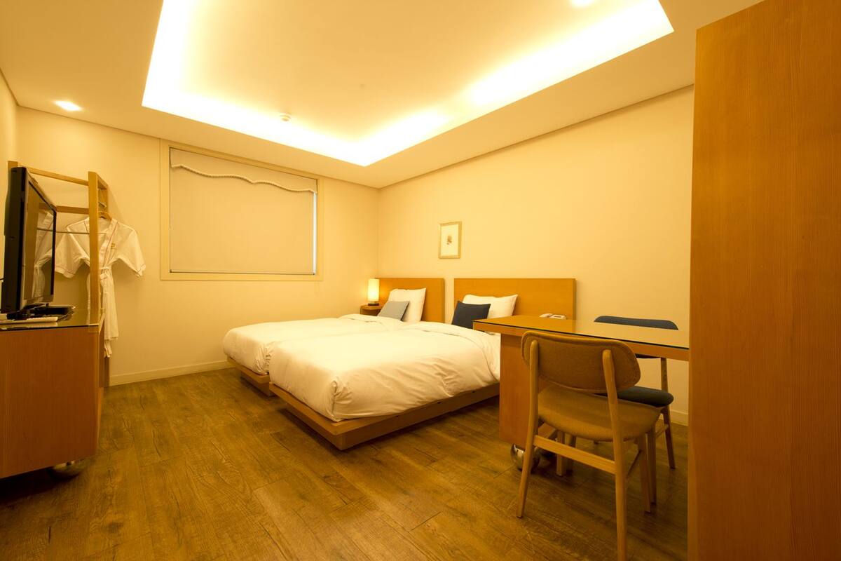 A hotel room with a bed, a desk, a chair, a mirror, and a television.