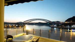 A balcony with a view of a bridge, a table, and two chairs. - Tongyeong Geobukseon Hotel (Tongyeong)