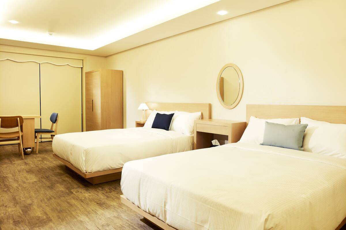 A hotel room with two beds, a desk, a chair, and a wardrobe.