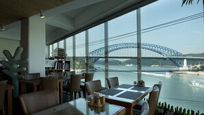 A restaurant with a view of a bridge over water, featuring a glass table and chairs. - Tongyeong Geobukseon Hotel (Tongyeong)