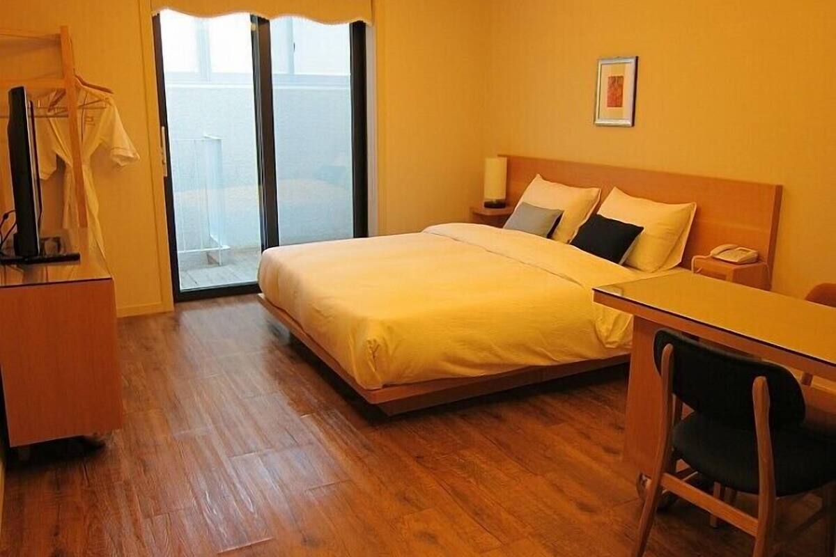 A hotel room with a bed, a desk, a chair, a wardrobe, and a door leading to a balcony.