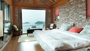 A bedroom with a large bed, a brick wall, a view of the sea, and a wooden floor. - Tongyeong Geobukseon Hotel (Tongyeong)