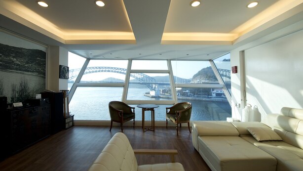 A modern interior with a large window overlooking a bridge and water, featuring a sofa, two chairs, and a small table. - Tongyeong Geobukseon Hotel (Tongyeong)