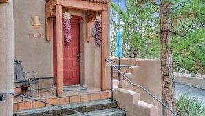 Un edifici amb una porta vermella, seients a l'exterior i una escala que condueix a una zona coberta.