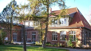 A two-story brick building with a red-tiled roof, a covered porch, and a stone pathway leading to the entrance. - 3) Holiday apartment 4-room, upper floor, 110m² - Landhaus Alte Schule near (Alt Bukow)