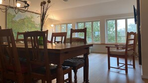 A dining room with a wooden table and chairs, a chandelier, and large windows with a view of trees. - 3) Holiday apartment 4-room, upper floor, 110m² - Landhaus Alte Schule near (Alt Bukow)