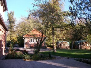 A brick building with a small shed, a wooden deck, and a stone wall with stacked firewood.