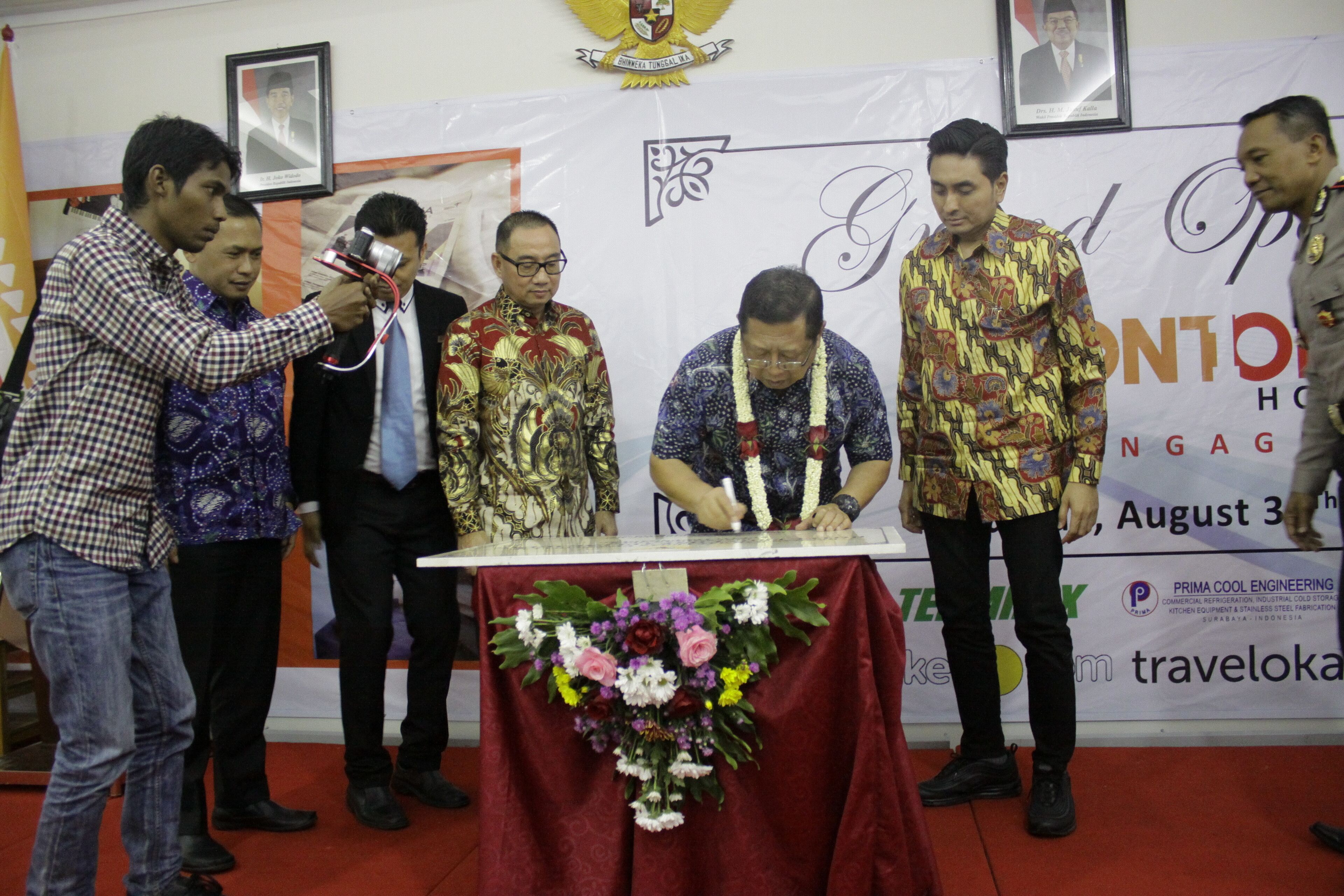 A group of people at a ceremony with a table decorated with flowers and a banner in the background.