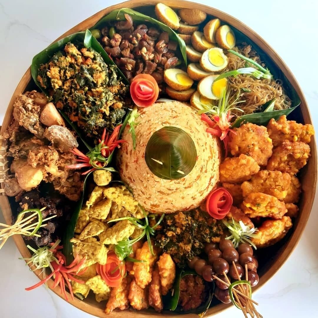 Un grand plateau de service rond en bois, rempli de divers plats, notamment des aliments frits, des légumes et un élément décoratif central.