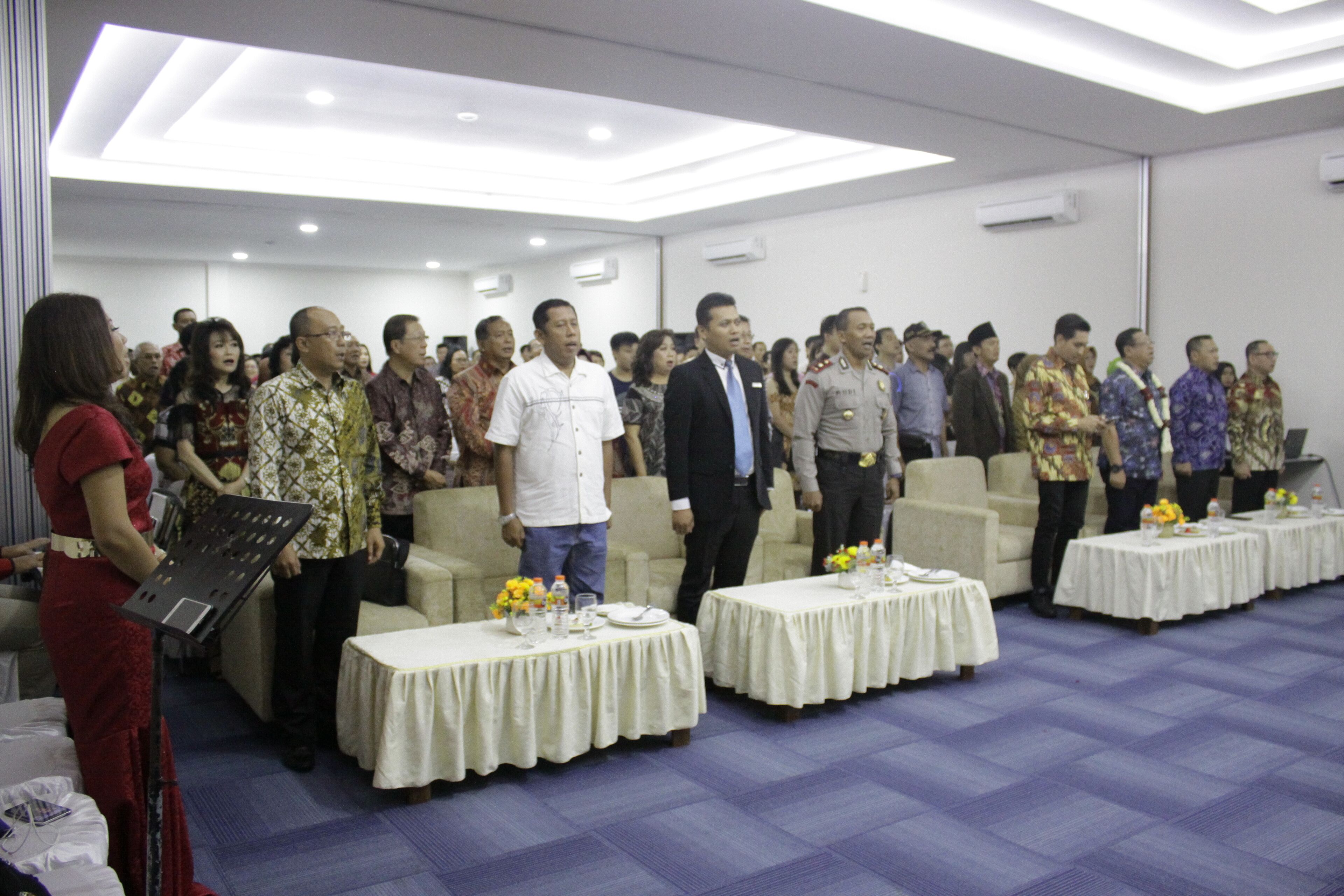 A conference room with a stage, tables with floral centerpieces, and a group of people standing.