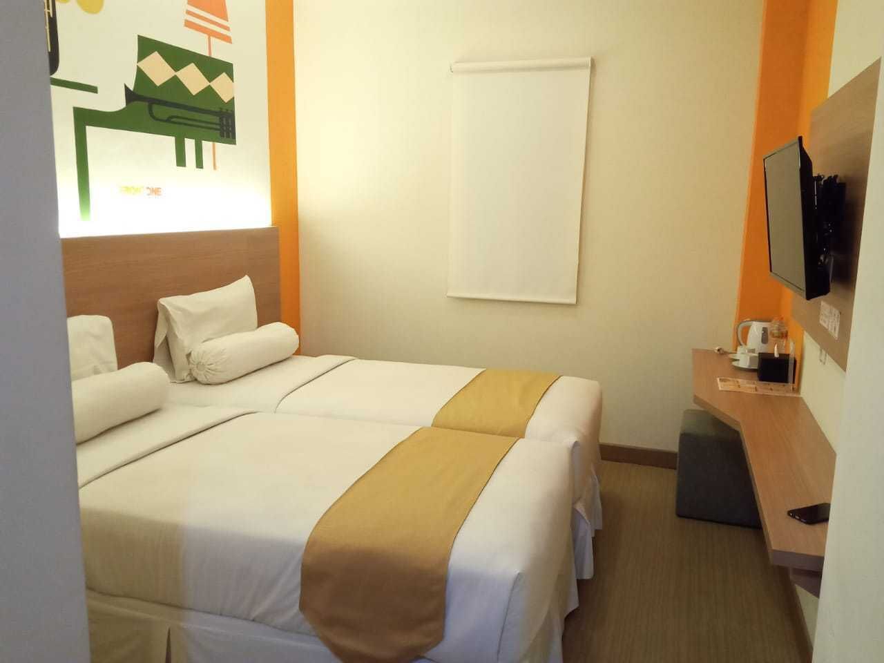 Habitación de hotel con dos camas, un escritorio, un televisor y ventana con vista a un edificio.