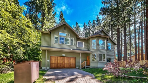 A two-story house with a garage, surrounded by trees and a brick driveway.