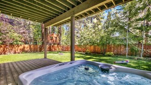A hot tub in a backyard with a wooden deck and a wooden fence.