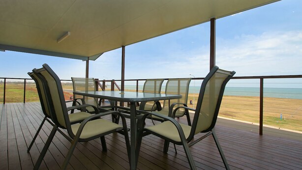 A covered outdoor dining area with a table and chairs, overlooking a beach. - 17 Sea Esplanade, Elliott Heads (ELLIOTT HEADS)