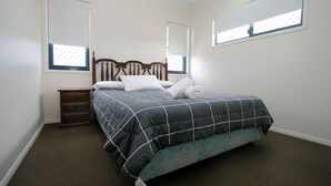 A bedroom with a bed, wooden headboard, a nightstand, and two windows. - 17 Sea Esplanade, Elliott Heads (ELLIOTT HEADS)