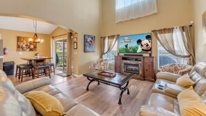 Een ruime woonkamer met een leren bank, een houten salontafel en een televisie waarop Mickey Mouse Clubhouse te zien is.
