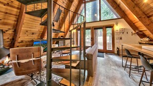 A wooden interior with a spiral staircase, a fireplace, and a dining area with a view of the outdoors. - Külhaus Cabin - Romantic A-frame Adventure, BBQ (South Lake Tahoe)