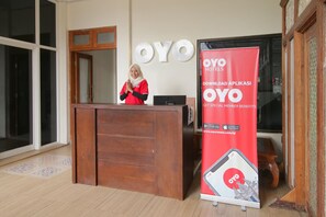 A reception desk with a wooden finish, a receptionist in a red uniform, and a large red banner advertising the OYO Hotels app.