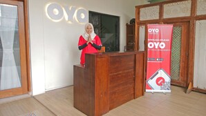 Un comptoir d’accueil avec un revêtement en bois, une personne derrière, et une grande bannière rouge faisant la publicité des hôtels OYO.