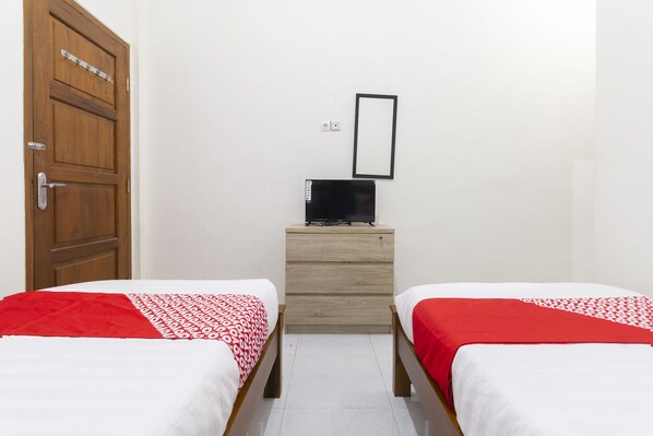 A room with two single beds, a wooden dresser, a black TV on the dresser, and a wooden door. - OYO 700 Griya Hanum Syariah (Depok)