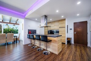 Een moderne keuken met een centraal eiland, barkrukken en een eethoek met rieten stoelen.