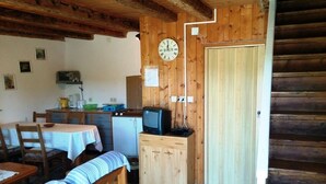 L’intérieur chaleureux d’un chalet avec des murs en bois, un coin repas comprenant une table et des bancs, une petite kitchenette et un téléviseur posé sur un meuble.