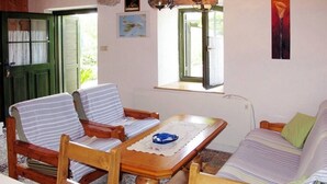Une pièce chaleureuse avec une table en bois, deux chaises à rayures, un canapé et une fenêtre avec des volets.