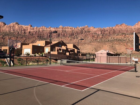 Una cancha de tenis con superficie roja, rodeada de edificios y un paisaje desértico.