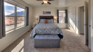 Un dormitorio con una cama grande, un ventilador de techo, vistas del desierto a través de la ventana y una puerta que da a otra habitación.