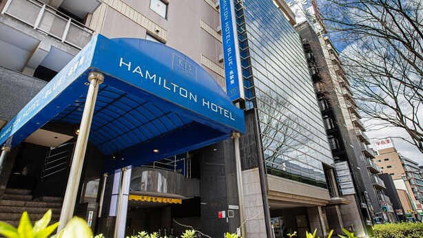 Exterior do Hotel Hamilton, com toldo azul e fachada de vidro moderna.