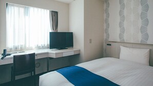 Quarto de hotel com cama, escrivaninha com computador, cadeira e televisão.