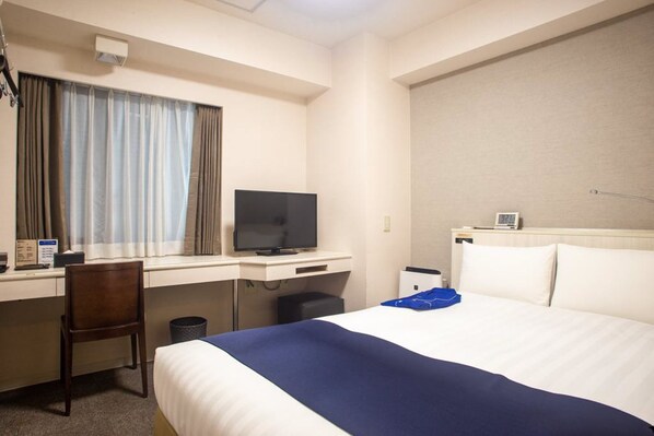 Une chambre d’hôtel avec un lit, un bureau avec une télévision, une chaise et une fenêtre avec des rideaux.
