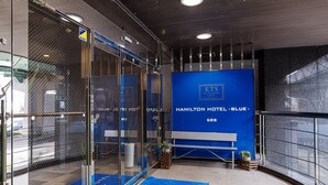 Um hall de hotel moderno com carpete azul, um balcão de recepção e uma grande parede azul com o nome do hotel.