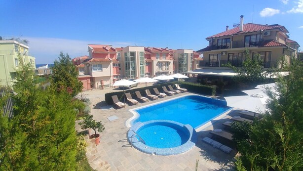 A swimming pool with lounge chairs and umbrellas, surrounded by buildings with red-tiled roofs and balconies. - Hotel Muses (Sozopol)