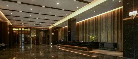 A modern lobby with a marble floor, a reception desk, and a wall with vertical wooden panels.
