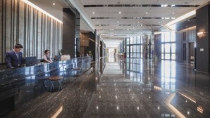 Un lobby moderno de hotel con una mesa de recepción, zona de estar y ventanas grandes.
