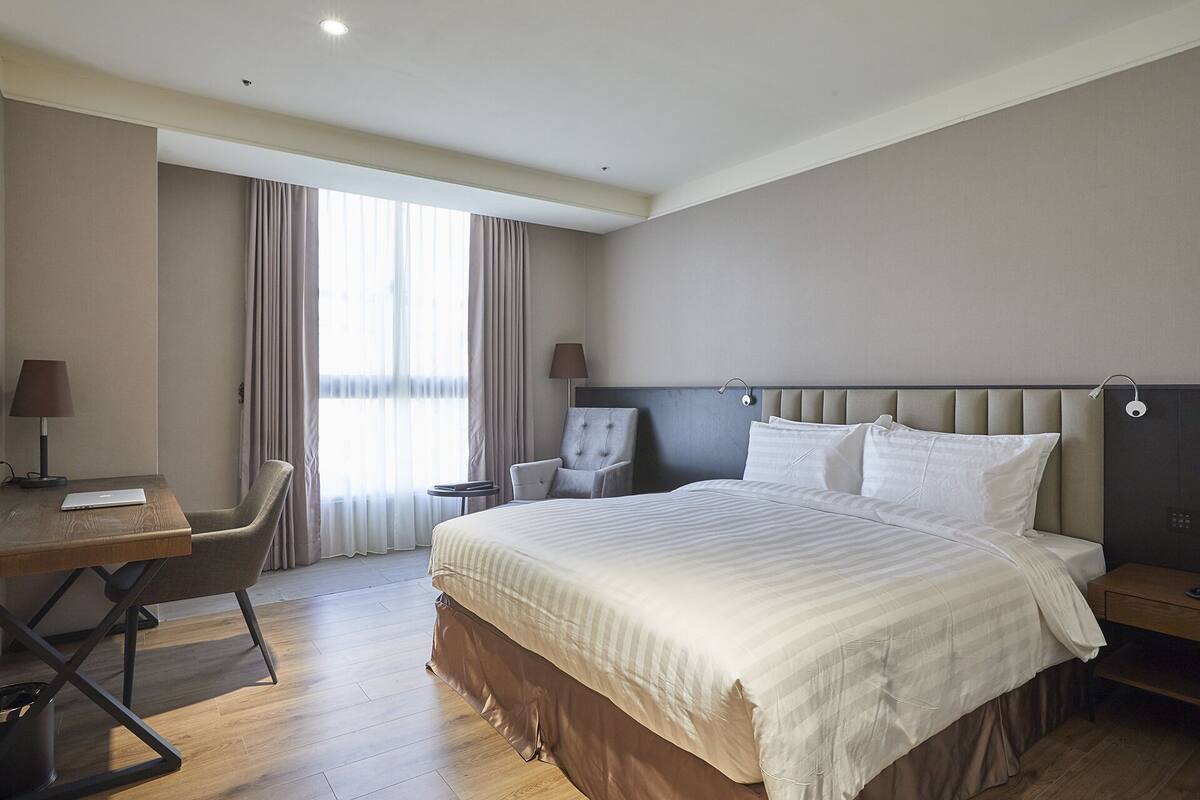 Una camera d'albergo con un letto grande, una scrivania con un portatile, una sedia e un tavolino.