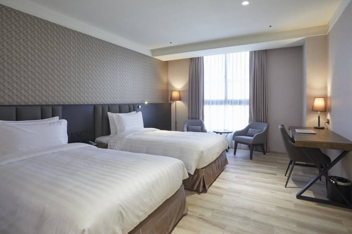 Camera d'albergo con due letti, una scrivania, una sedia e vista sull'esterno.