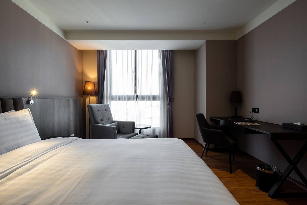 Una camera d'albergo con un letto grande, una scrivania, una sedia e una finestra con tende.