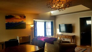 A living room with a painting, a chandelier, a television, and a view of the outdoors. - Gowdy Apartment. Fenced yard pet friendly , modern, clean. Gowdy Properties (Lake City)