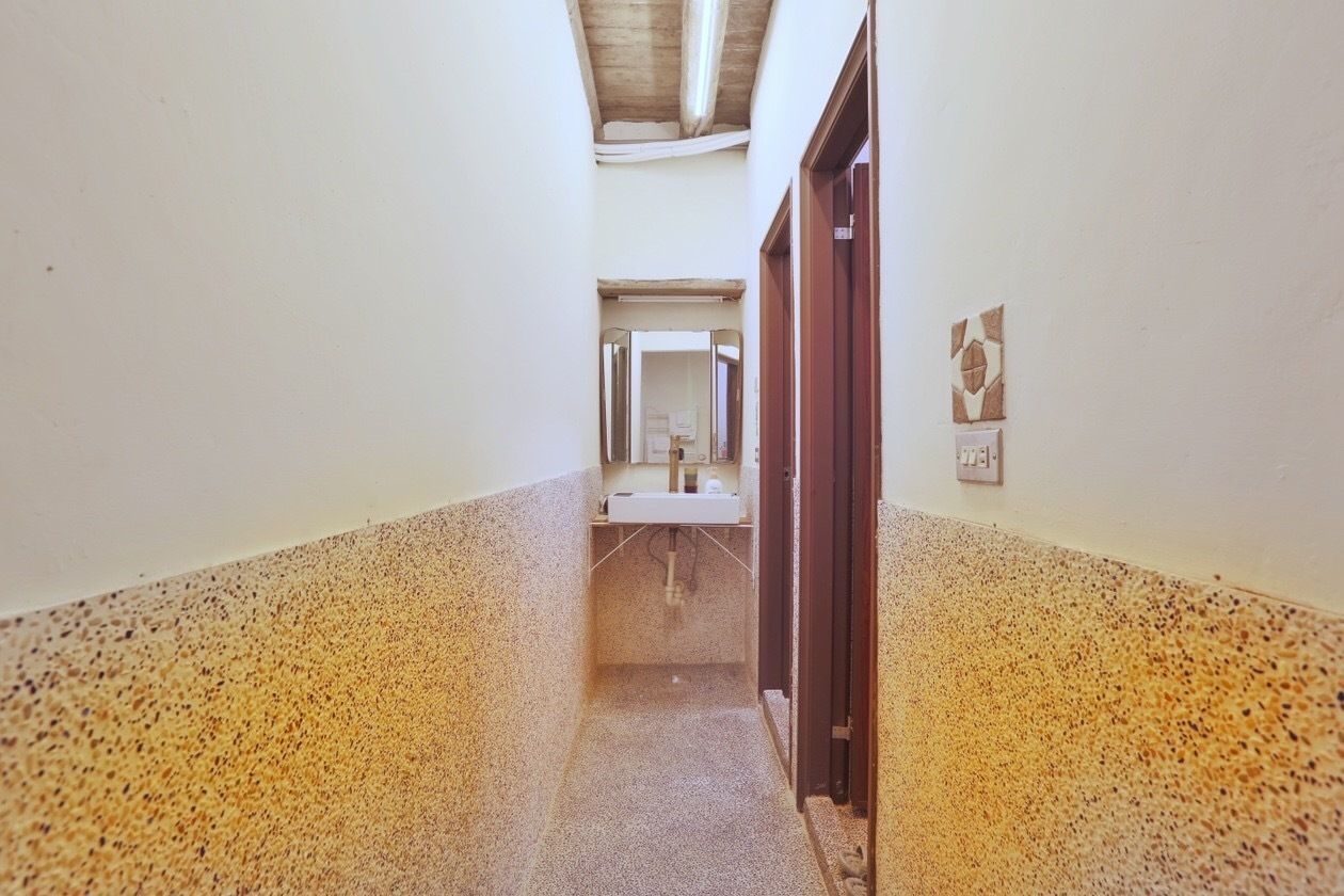 A narrow hallway with a speckled floor, a sink, and a mirror at the end.