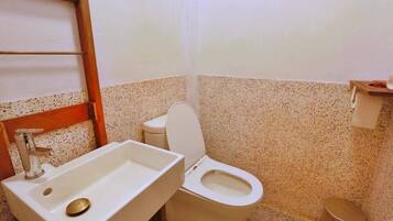 Un baño con lavamanos blanco, un inodoro y un cubo de basura.