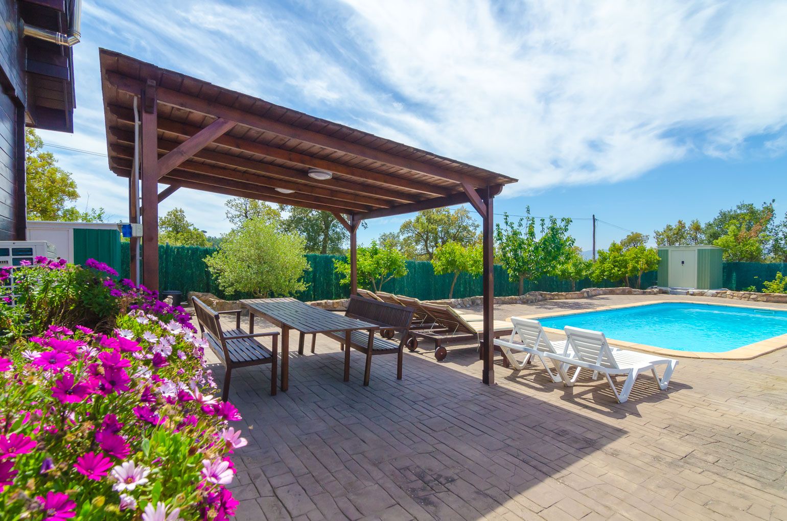 Ein überdachter Außenbereich mit Pool, Liegestühlen und einer Pergola.