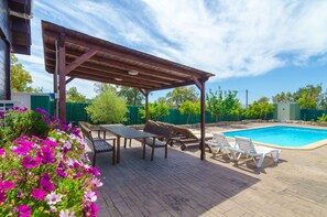 Un espacio exterior techado con piscina, sillas de descanso y una pérgola.