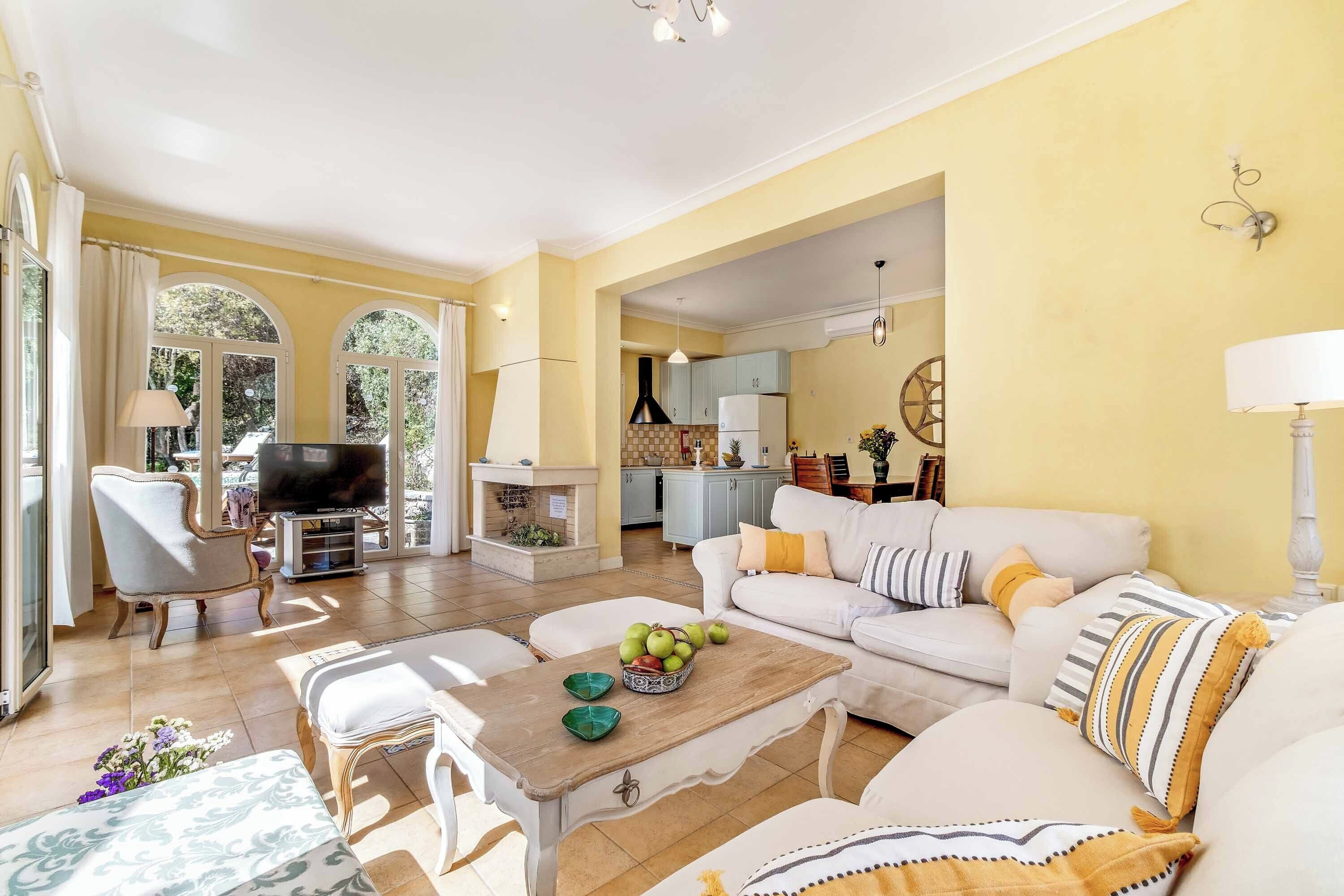 Amplia sala de estar con sofá, mesa de centro y televisor. Se ve una cocina al fondo.