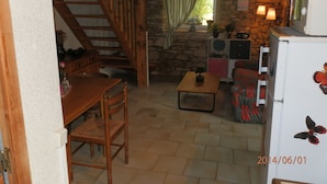 A cozy room with a wooden staircase, a stone wall, a small table with a plant, a sofa, and a refrigerator with a butterfly decal. - Two country cottages (restored barn), at the end of an old farm. (Puy-L'évêque)