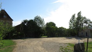 A gravel driveway leading to a stone building with a small window, surrounded by trees and greenery. - Two country cottages (restored barn), at the end of an old farm. (Puy-L'évêque)