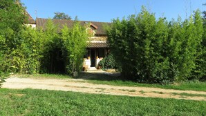 A traditional house with a tiled roof, surrounded by lush greenery and a clear blue sky. - Two country cottages (restored barn), at the end of an old farm. (Puy-L'évêque)