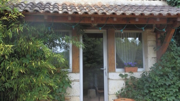 A stone house with a tiled roof, a wooden door, and a small porch with a wooden chair. - Two country cottages (restored barn), at the end of an old farm. (Puy-L'évêque)