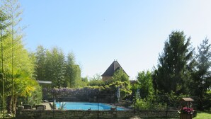 A swimming pool surrounded by lush greenery, a stone wall, and a building with a pyramid-shaped roof. - Two country cottages (restored barn), at the end of an old farm. (Puy-L'évêque)